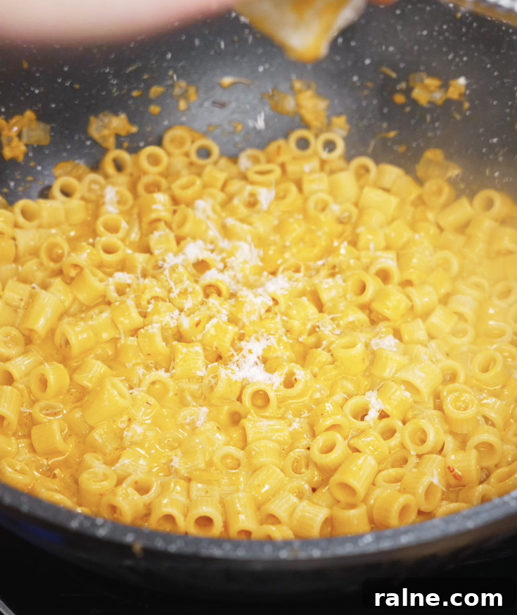 Freshly grated parmesan cheese is sprinkled over the finished chili oil vodka pasta while still in the pan.