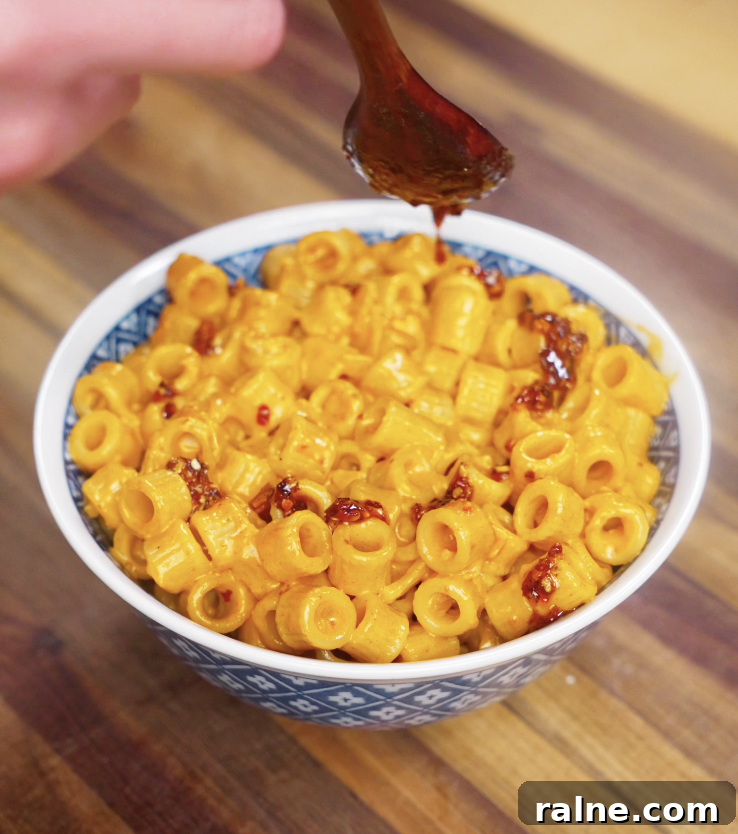 A hand drizzles chili oil over a bowl of creamy vodka pasta, adding a final layer of heat and flavor to the rich, golden sauce.