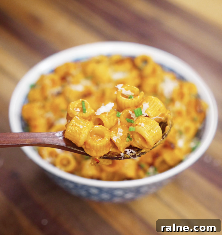 A wooden spoon lifting creamy chili oil vodka pasta from the bowl, showing the glossy sauce and bits of garnish.