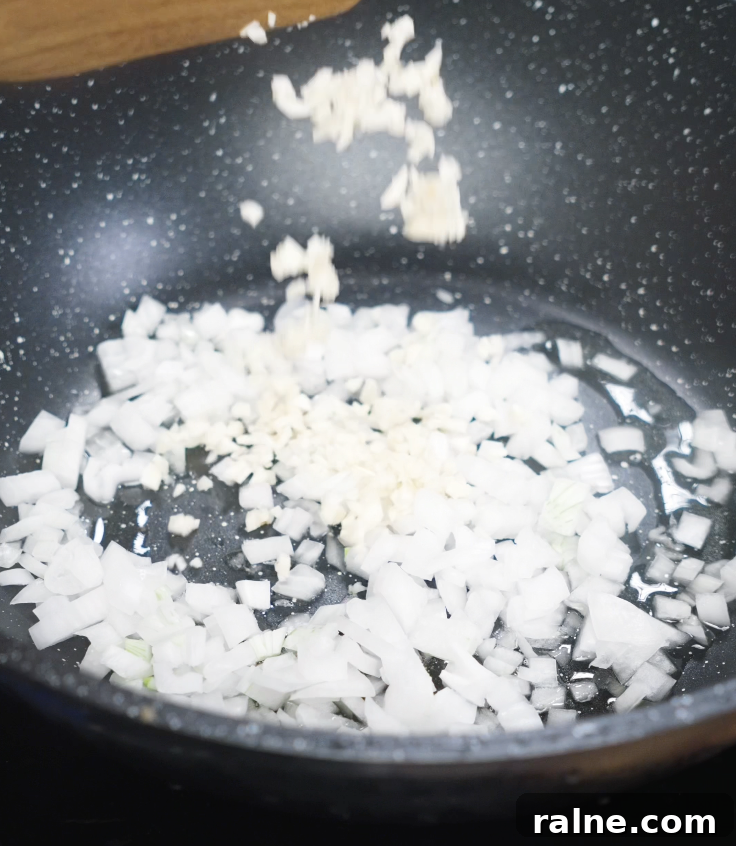 Diced white onions and minced garlic are sizzling in oil inside a nonstick pan to build the base for the sauce.