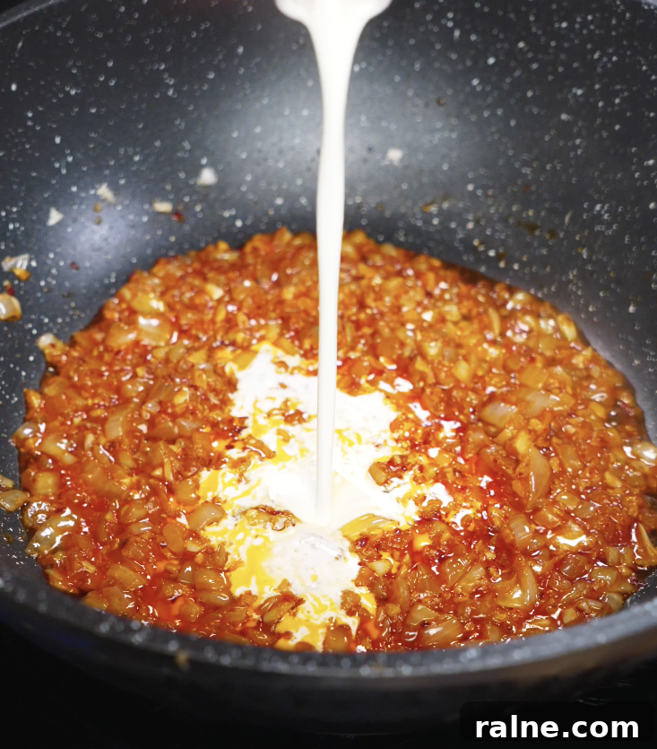 A stream of heavy cream is poured into the pan of aromatic chili tomato mixture to create a silky sauce.