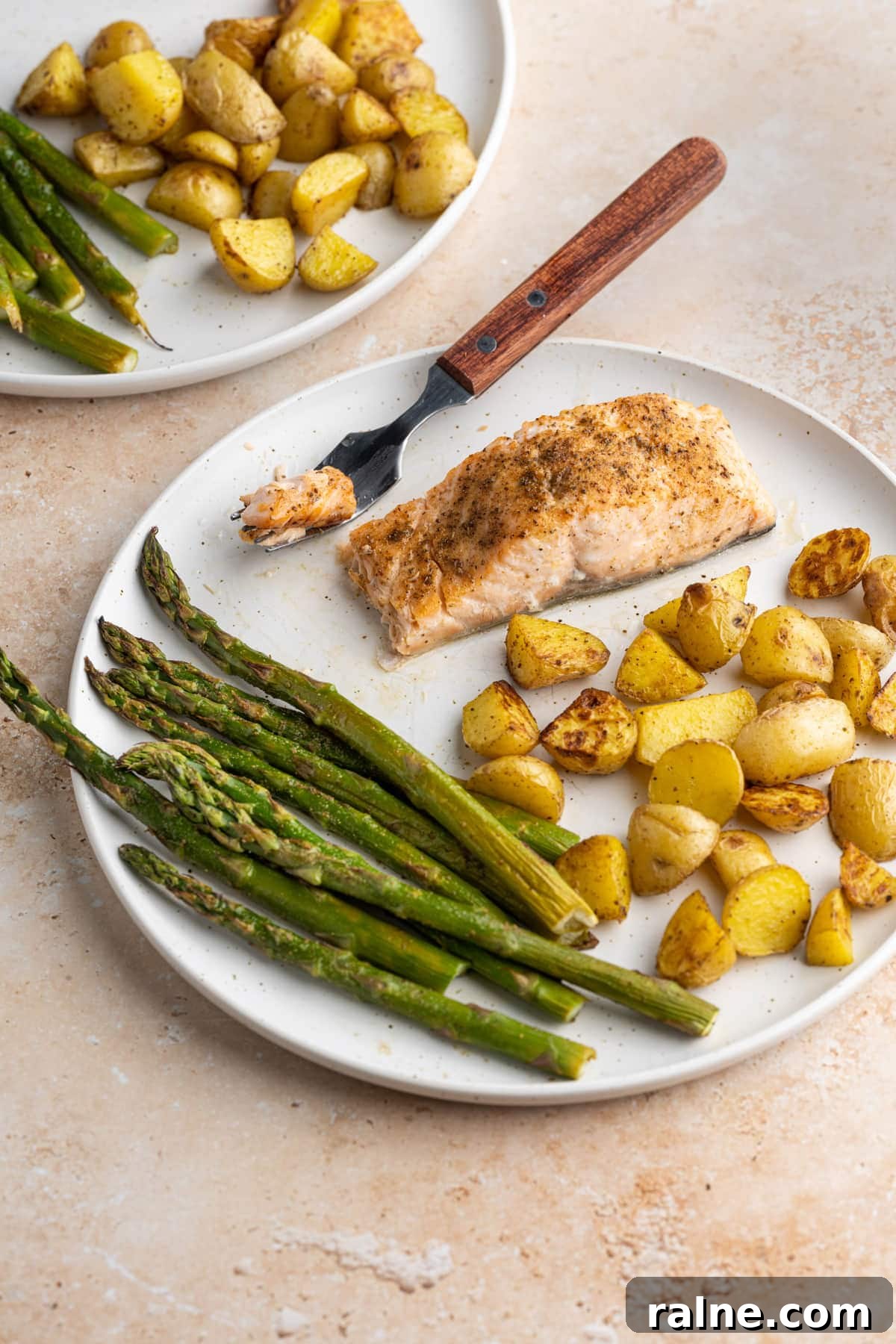 Salmon with forkful cut out on plate with asparagus and potatoes
