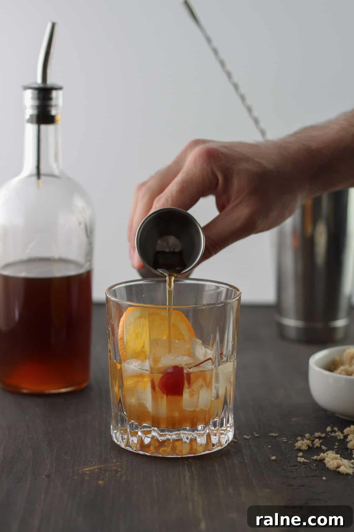 Brown Sugar Simple Syrup Recipe for Cocktails and Coffee 3 A brown sugar old fashioned cocktail with a hand pouring in brown sugar simple syrup.