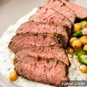 Marinated Lamb Backstrap Recipe: Juicy Grilled Lamb Backstrap 8 Round grey plate with a serving of sliced Lamb Backstrap, sitting on yoghurt sauce, with a chickpea cucumber side salad.