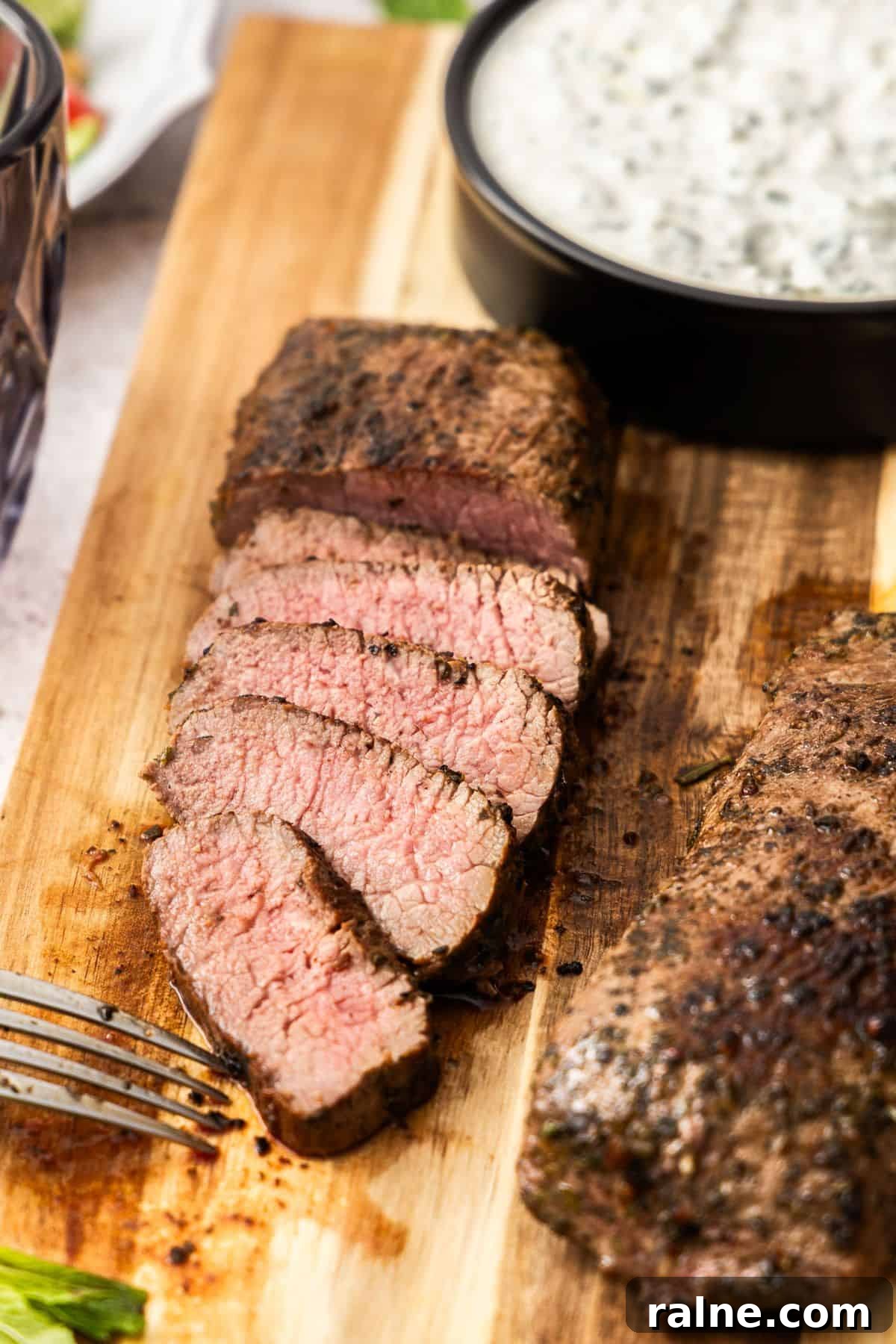 Marinated Lamb Backstrap Recipe: Juicy Grilled Lamb Backstrap 4 Wooden board, with dish of yoghurt sauce and two lamb backstraps, one slice into pieces.