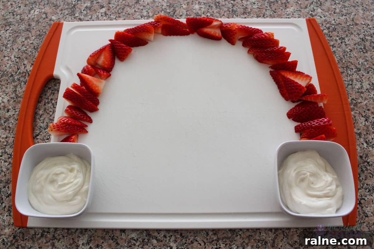 Colorful Fruit Platter with Creamy Yogurt Dip 7 A cutting board on a counter with strawberries arching from one side up to the top and over to the other side, with yogurt dip in small bowls at the bottom of each side of the arch.