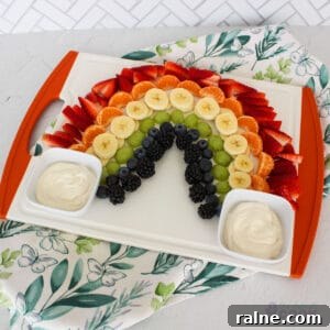 Colorful Fruit Platter with Creamy Yogurt Dip 9 A fruit platter arranged in a rainbow pattern on a white serving tray, with yogurt dips on either side, against a white tile background with a decorative napkin, and 'the default cook' watermark at the bottom right.