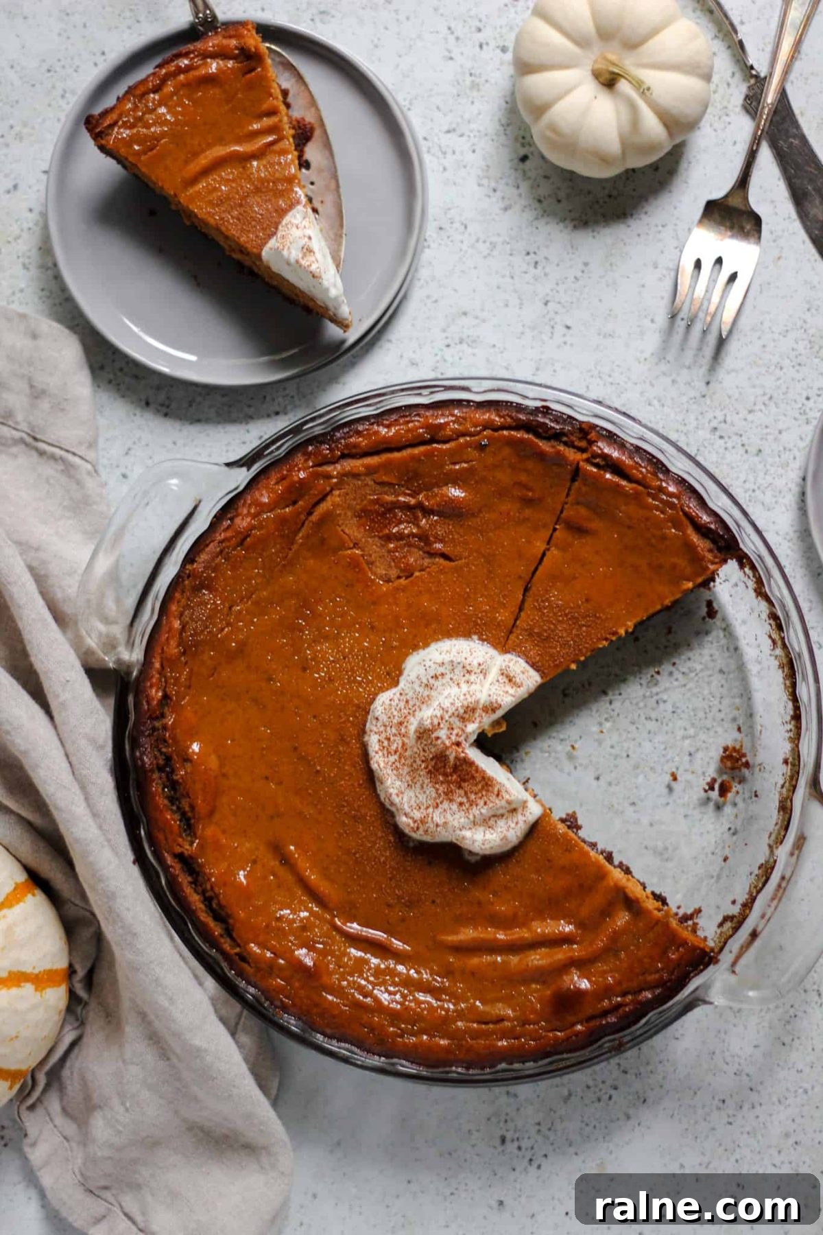 flatlay of pumpkin pie in a round glass dish with a slice of pie on a small grey plate