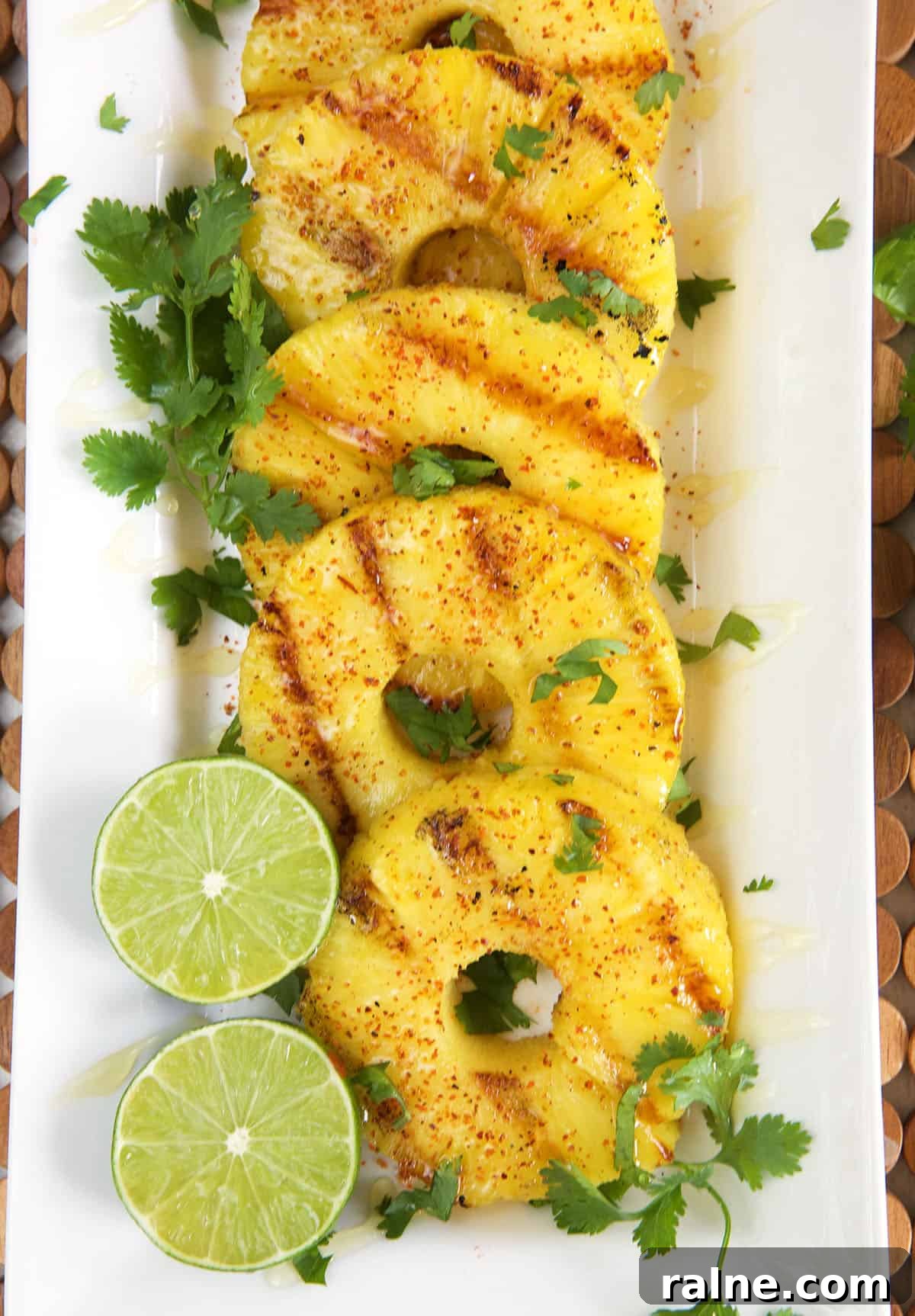Grilled Pineapple with Chili-Lime Glaze 2 Grilled pineapple on a white platter with sliced lime and chopped cilantro