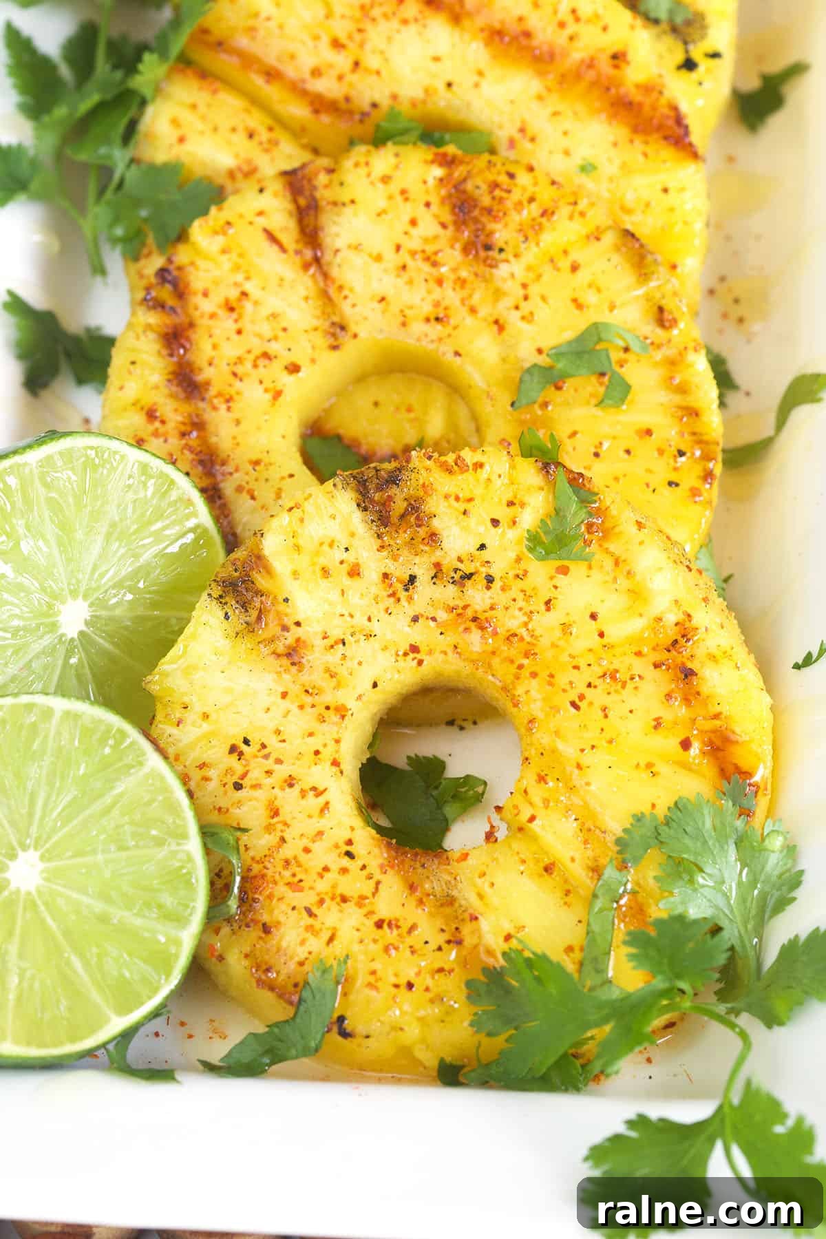 Grilled Pineapple with Chili-Lime Glaze 3 Three slices of grilled pineapple with cilantro sprigs and two lime slices.