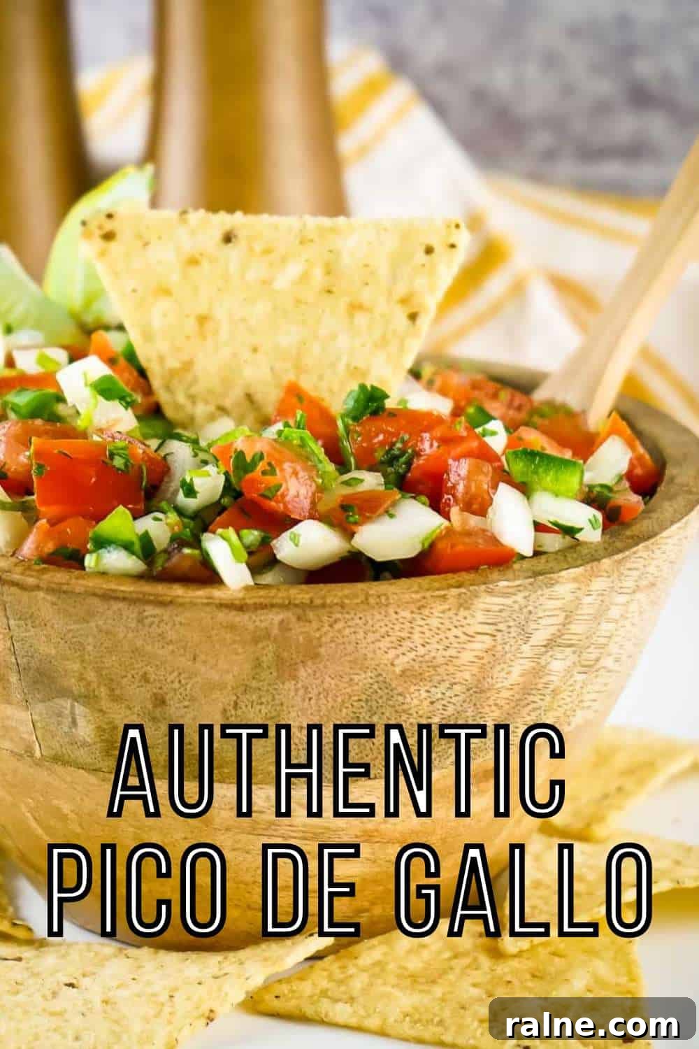 Authentic Mexican Pico de Gallo Recipe: Fresh Salsa Tradicional 2 Side shot of a tortilla chip, lime wedges, and a wooden spoon sticking out of a bowl of pico de gallo in a wooden bowl with more tortilla chips scattered around on a white surface.