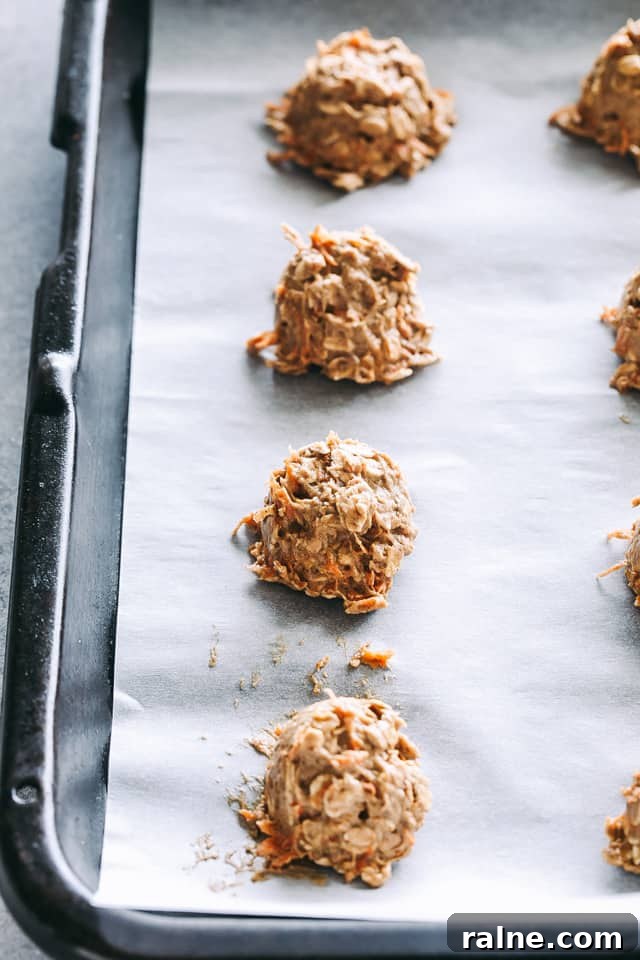 Unbaked oatmeal cookies with carrots arranged on a baking sheet.