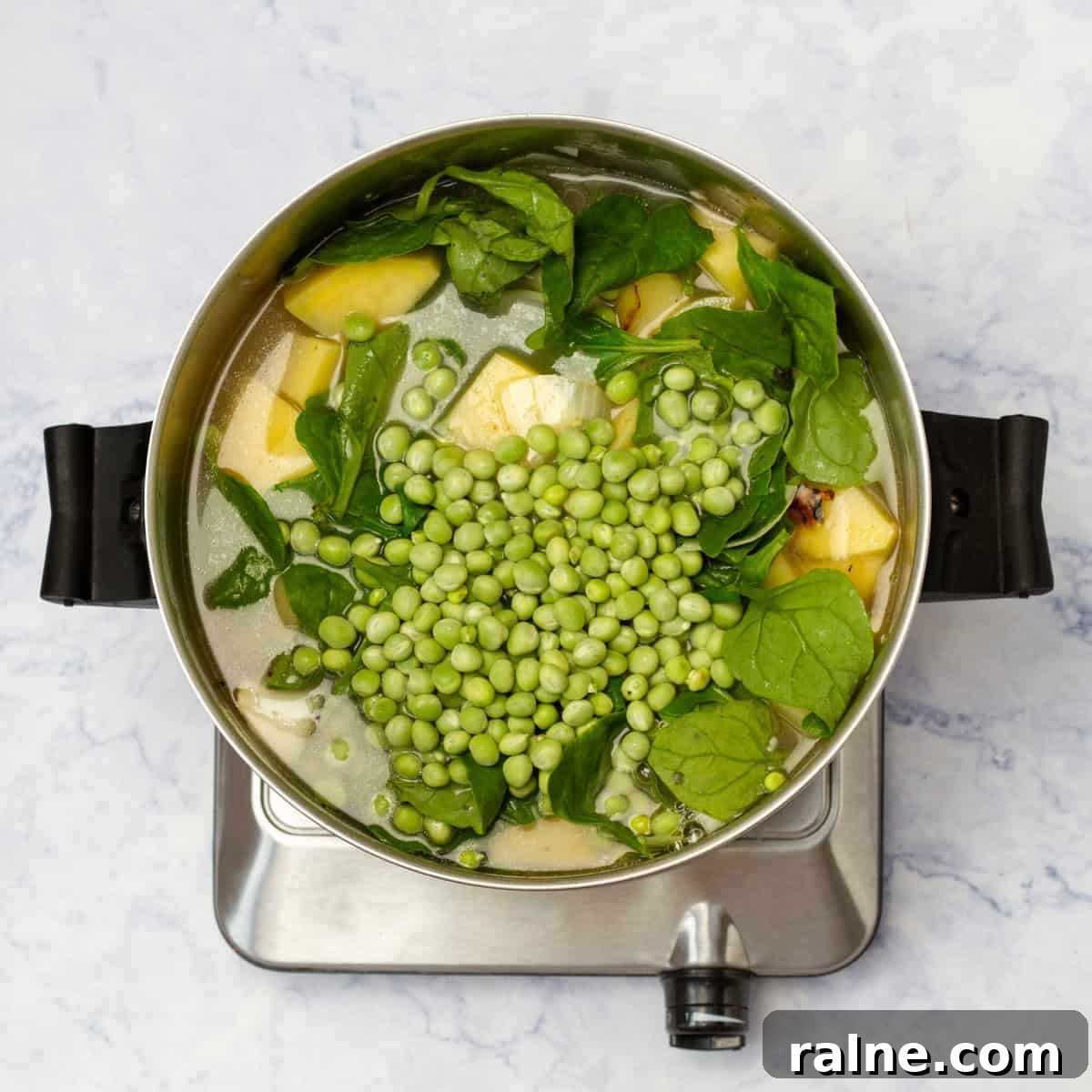 Sauteed onions, potatoes, spinach, and peas simmering in a pot with chicken broth.