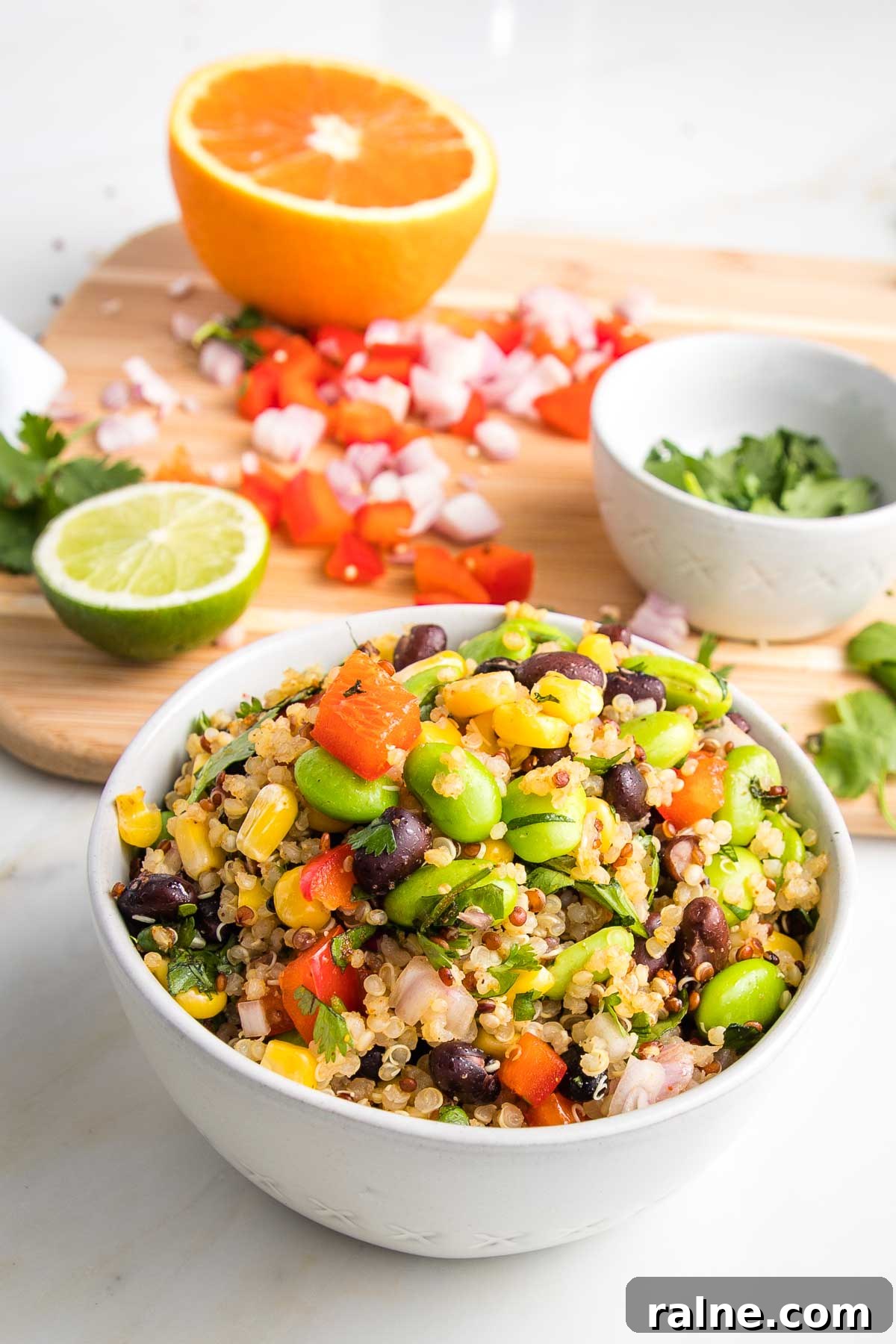 Southwest Quinoa Salad with Black Beans, Corn & Lime Dressing 9 Bowl of colorful veggies plus quinoa and in the background a cutting board with half an orange, half a lime, chopped red peppers and shallots and cilantro