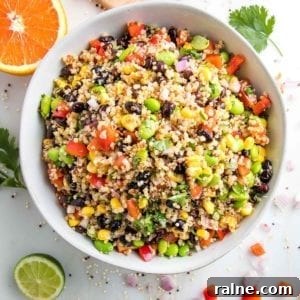 Southwest Quinoa Salad with Black Beans, Corn & Lime Dressing 10 close up photo of a large white bowl filled with colorful quinoa salad that includes red peppers, green edamame, black beans, bright yellow corn and chopped cilantro. There is an orange half and a half a lime, plus fresh cilantro leaves around the bowl.