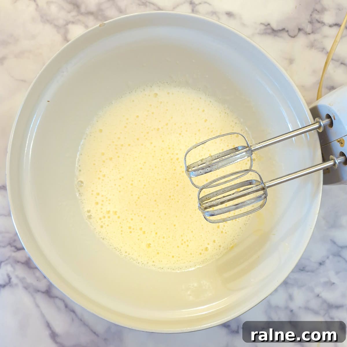 Light Mascarpone Strawberry Cake Without Butter — Moist Summer Dessert 5 Eggs and sugar whisked together in a mixing bowl. There is an electric beater on resting on the side of the mixing bowl.