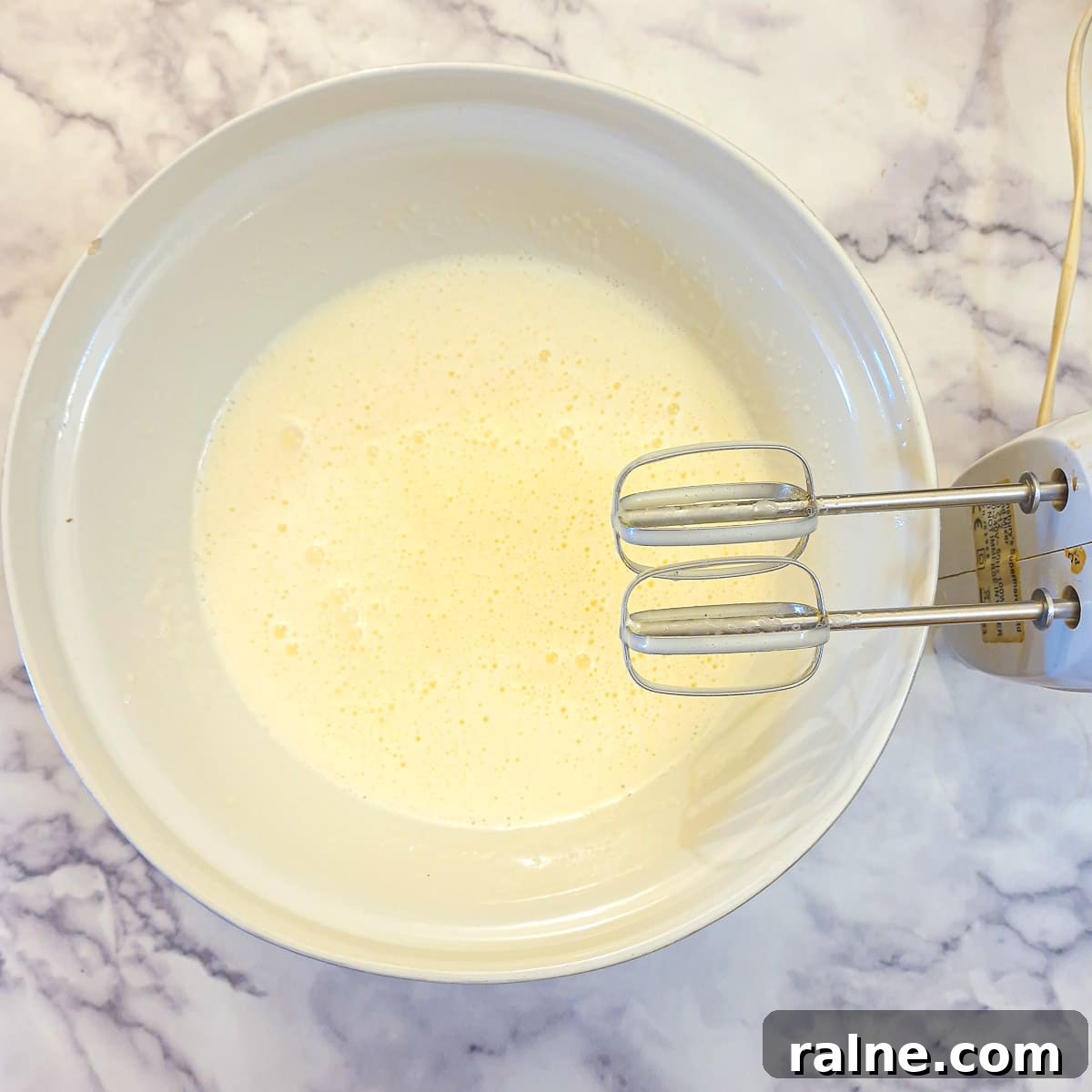 Light Mascarpone Strawberry Cake Without Butter — Moist Summer Dessert 6 A white mixing bowl showing mascarpone cheese whisked into the eggs and sugar with an electric hand mixer.