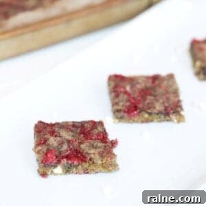 Raspberry White Chocolate Blondies with Crisp Edges and Gooey Center 9 Two Raspberry and White Chocolate Blondies on a white platter with a bar pan of blondies in the background.
