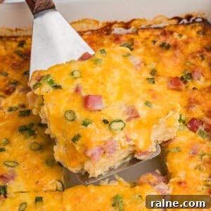 A slice of farmers casserole being lifted from the baking dish, highlighting its chunks of ham, bits of green onion, and golden melted cheese.