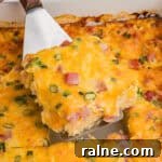 A slice of farmers casserole being lifted from the baking dish, highlighting its chunks of ham, bits of green onion, and golden melted cheese.