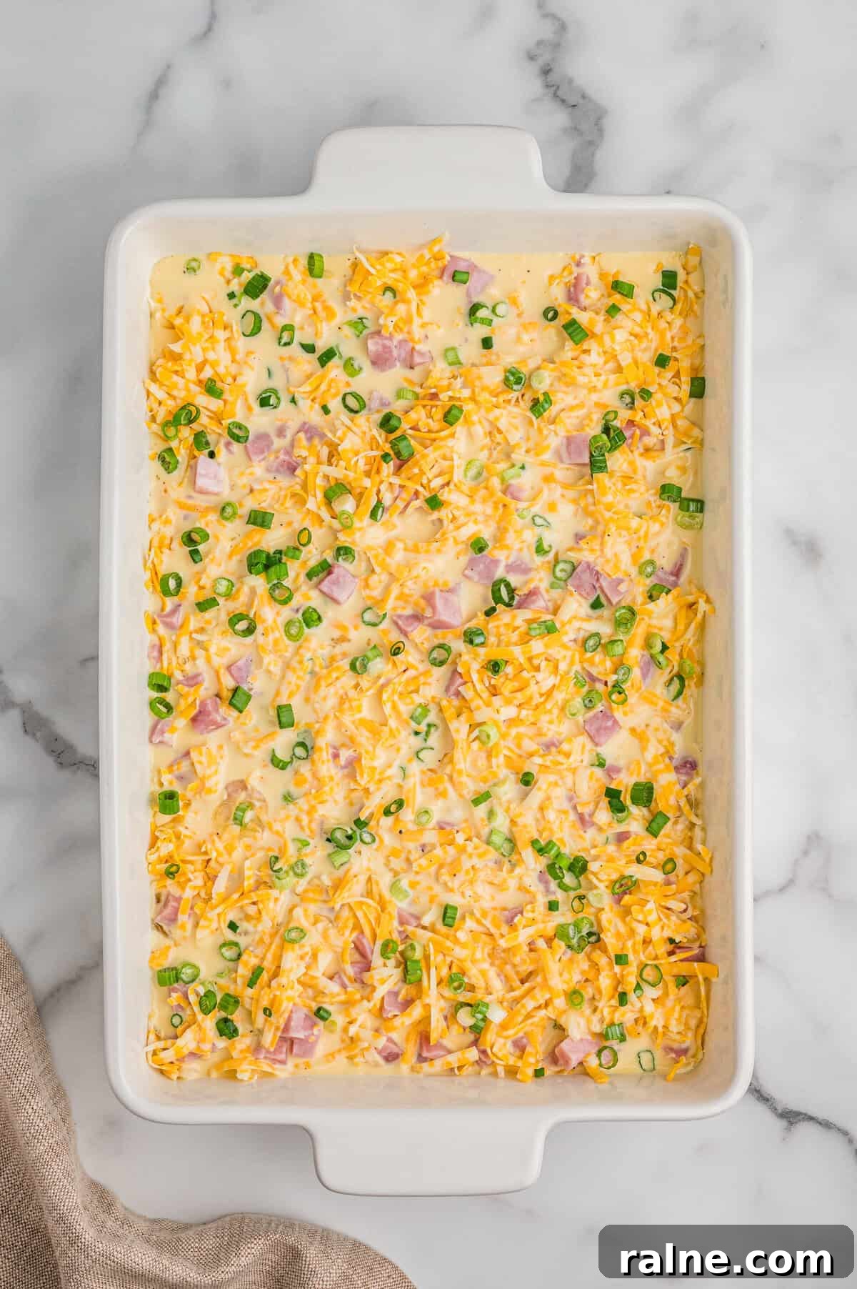 Breakfast casserole ingredients in casserole dish with egg mixture poured over them.