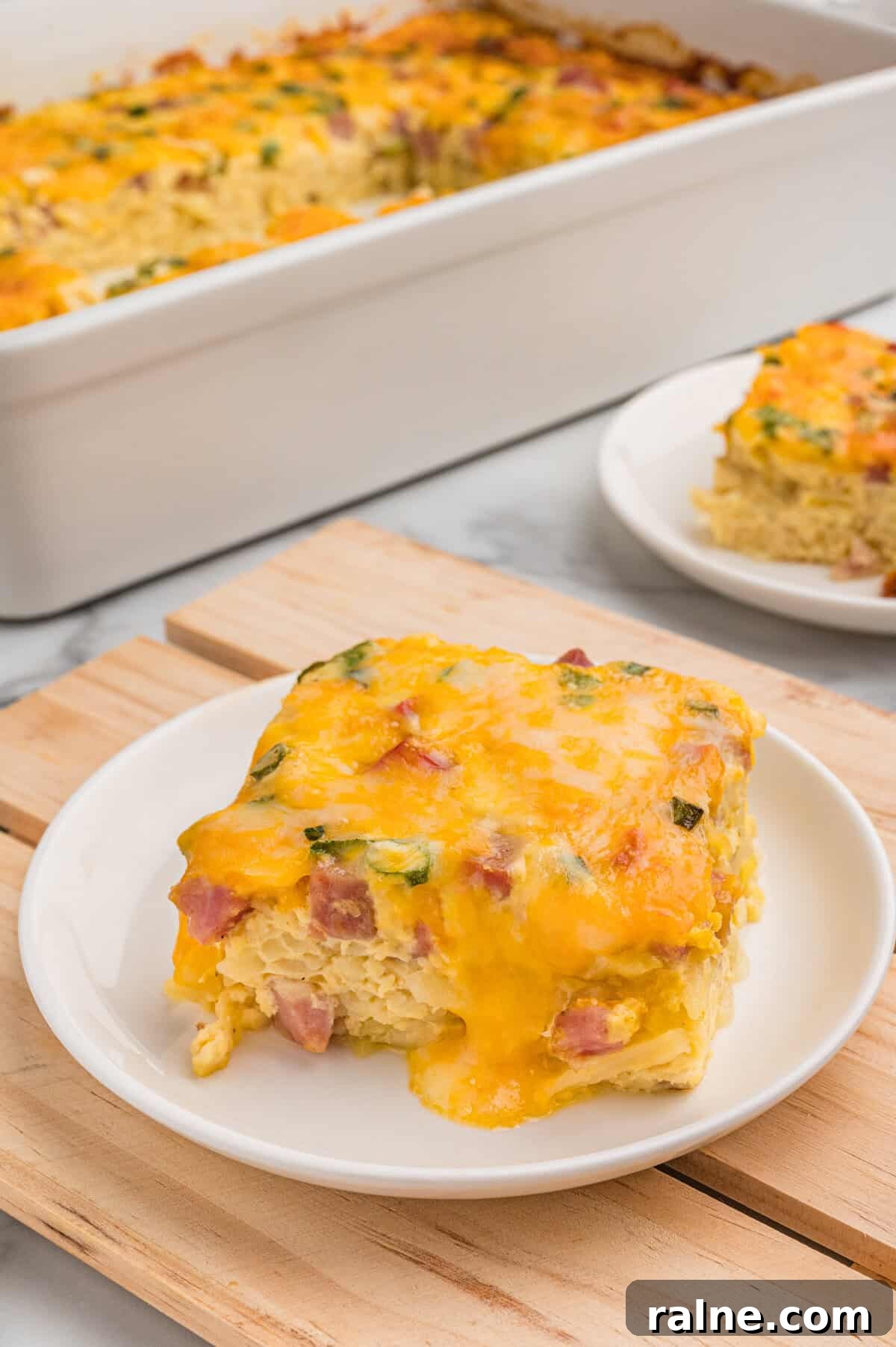 A slice of farmers casserole plated in front of the baking dish.