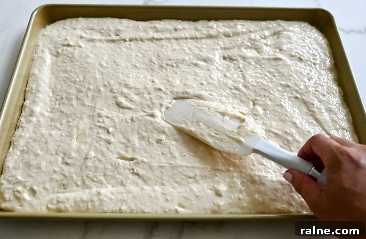 Spreading pancake batter into an even layer on a 9x13-inch baking sheet.
