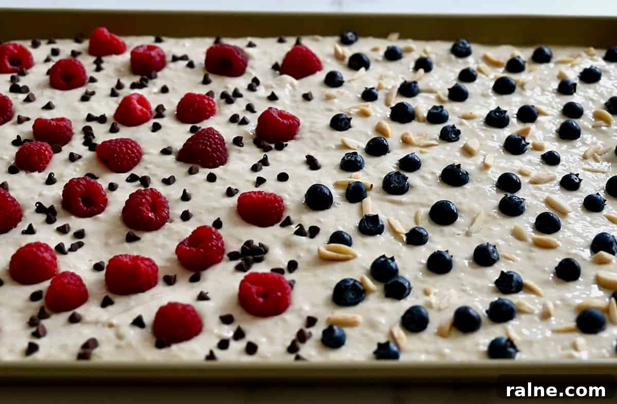 Berries, mini chocolate chips and nuts scattered atop pancake batter spread evenly on a baking sheet.