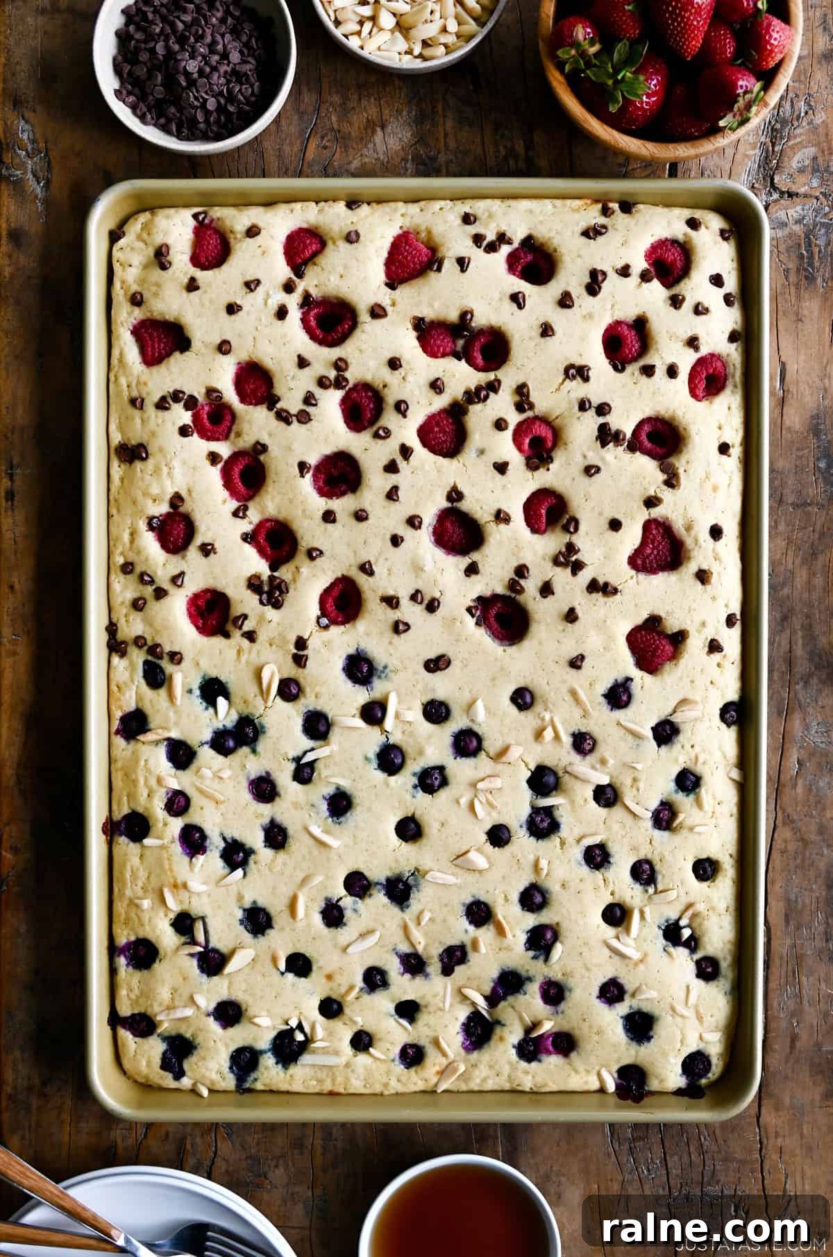 Sheet pan pancakes with blueberries on one half and raspberries and mini chocolate chips on the other half.