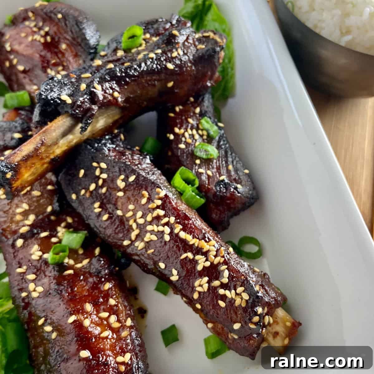Sticky Asian-Style Pork Spareribs Recipe 4 Asian sticky ribs in white serving dish garnished with chives.