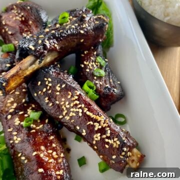 Sticky Asian-Style Pork Spareribs Recipe 5 Asian sticky ribs in white serving dish garnished with chives.