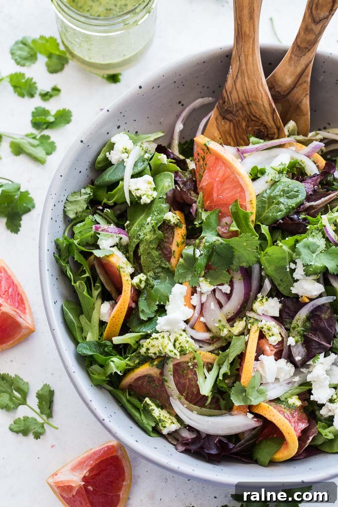 Overhead view of Grapefruit Salad with Cilantro and Goat Cheese in a grey bowl with wooden serving spoons.