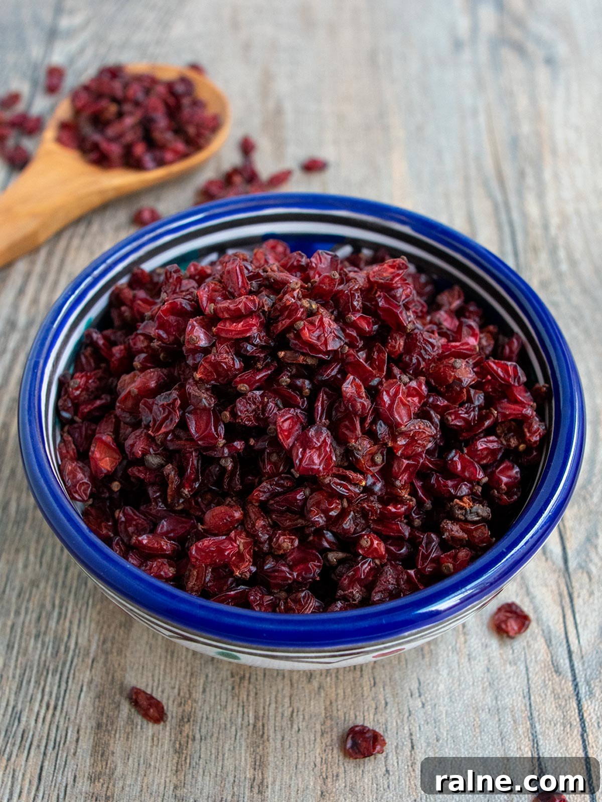 Barberries (Zereshk): A Culinary Guide to Persia’s Tangy Jewel 2 Blue bowl of barberries with a wooden spoon in the background.