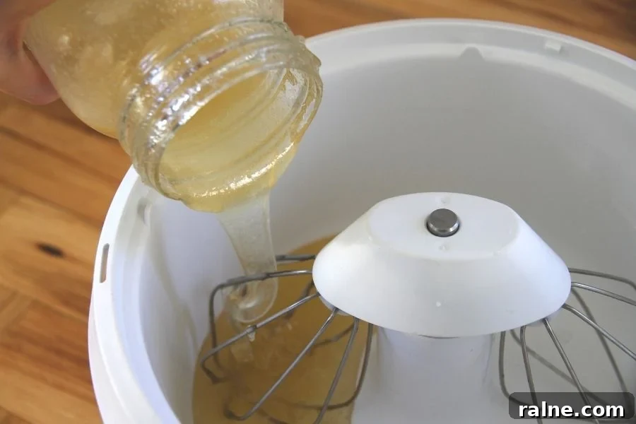 How to Make Smooth Creamed Honey at Home 3 raw liquid honey being poured from a jar into a kitchen mixer