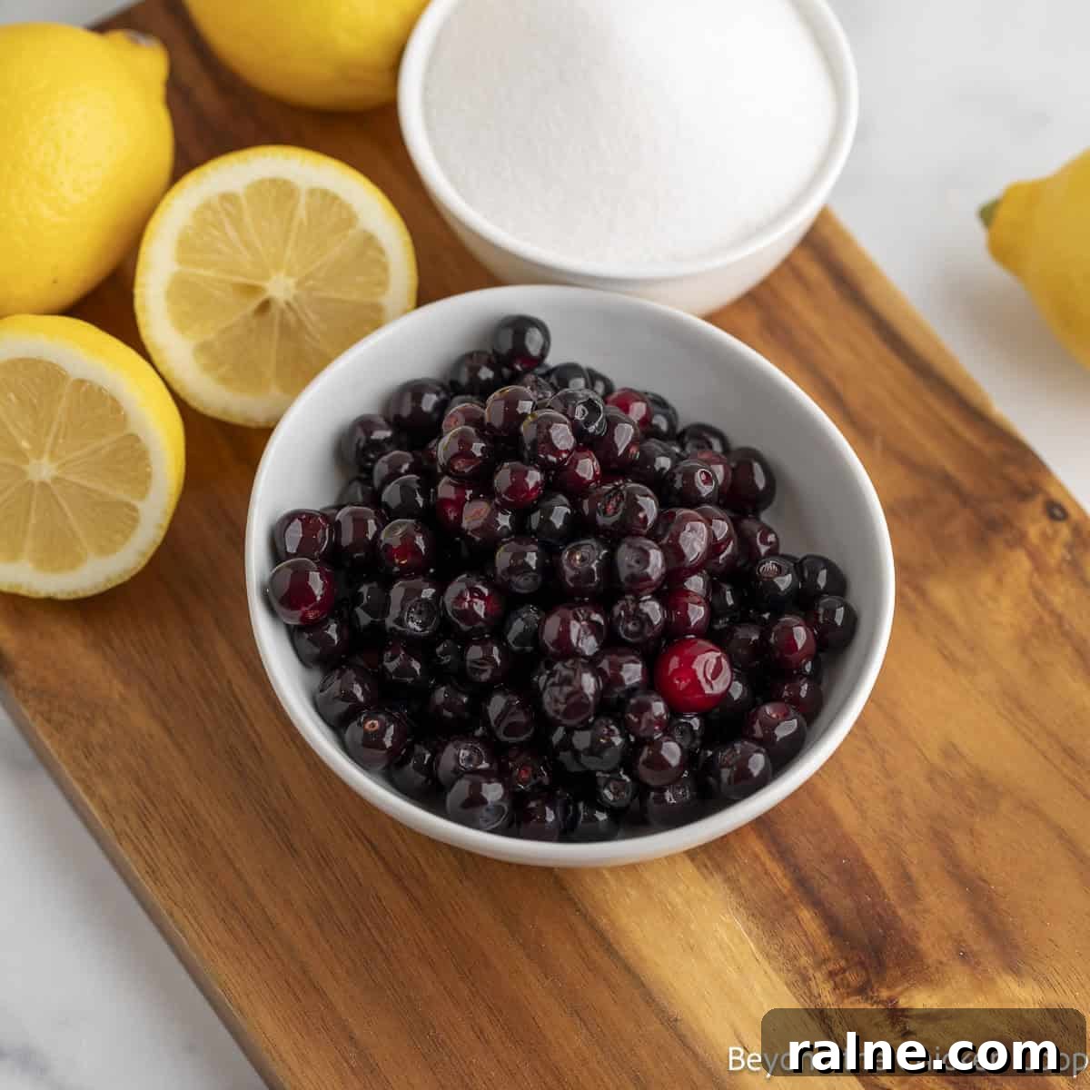 Huckleberry Lemonade Recipe: Refreshing Summer Drink with Fresh Berries 4 A bowl of fresh huckleberries, a bowl of sugar, and fresh lemons on a wooden board.