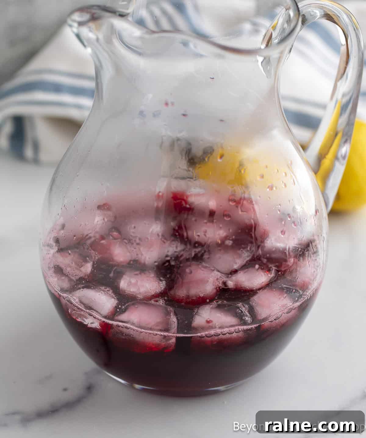 Huckleberry Lemonade Recipe: Refreshing Summer Drink with Fresh Berries 8 Huckleberry syrup in a glass pitcher with ice.
