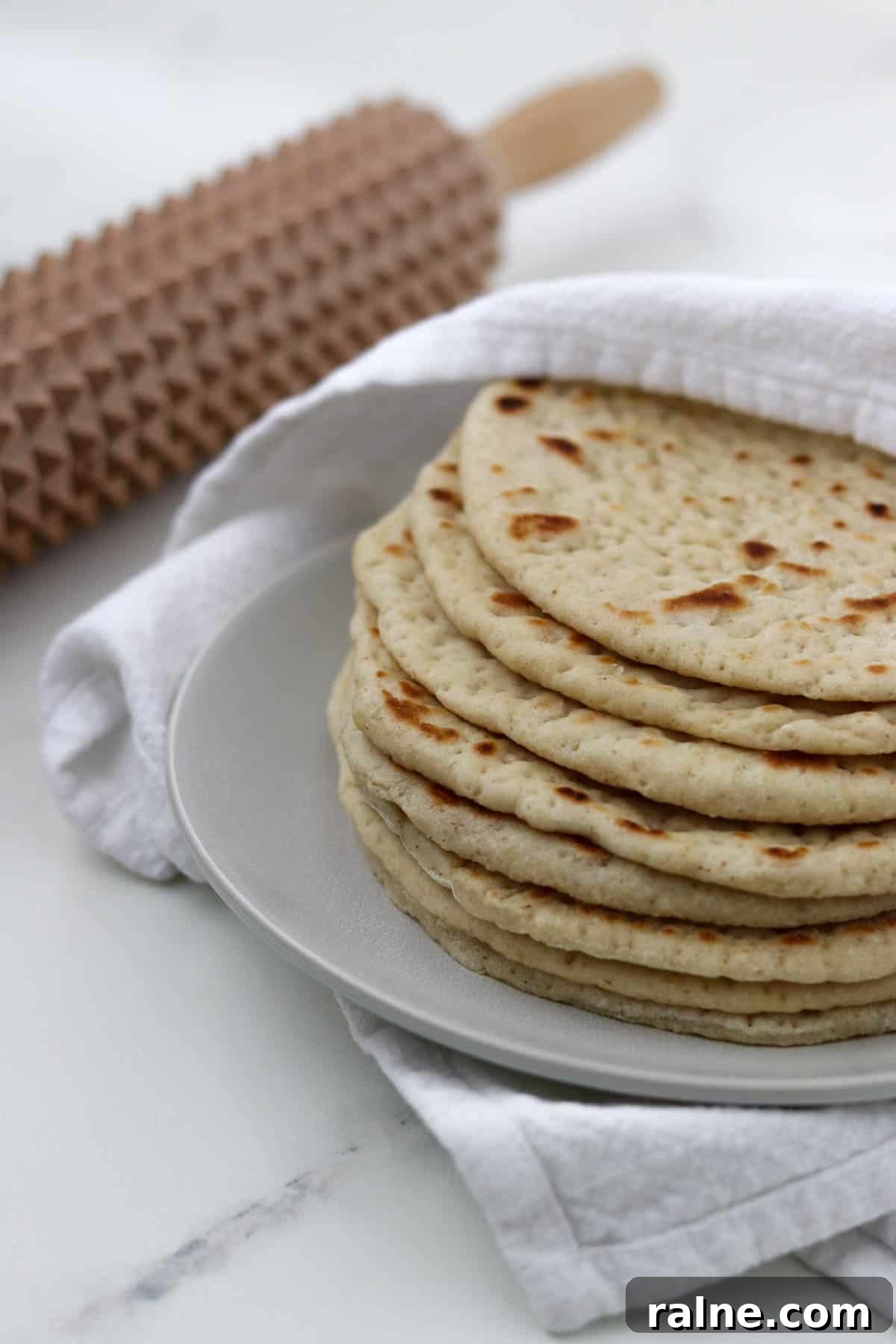 Soft Swedish Tunnbröd Recipe: How to Make Traditional Flatbreads 2 Soft Swedish Flatbreads on a plate next to a towel and a spiky rolling pin.