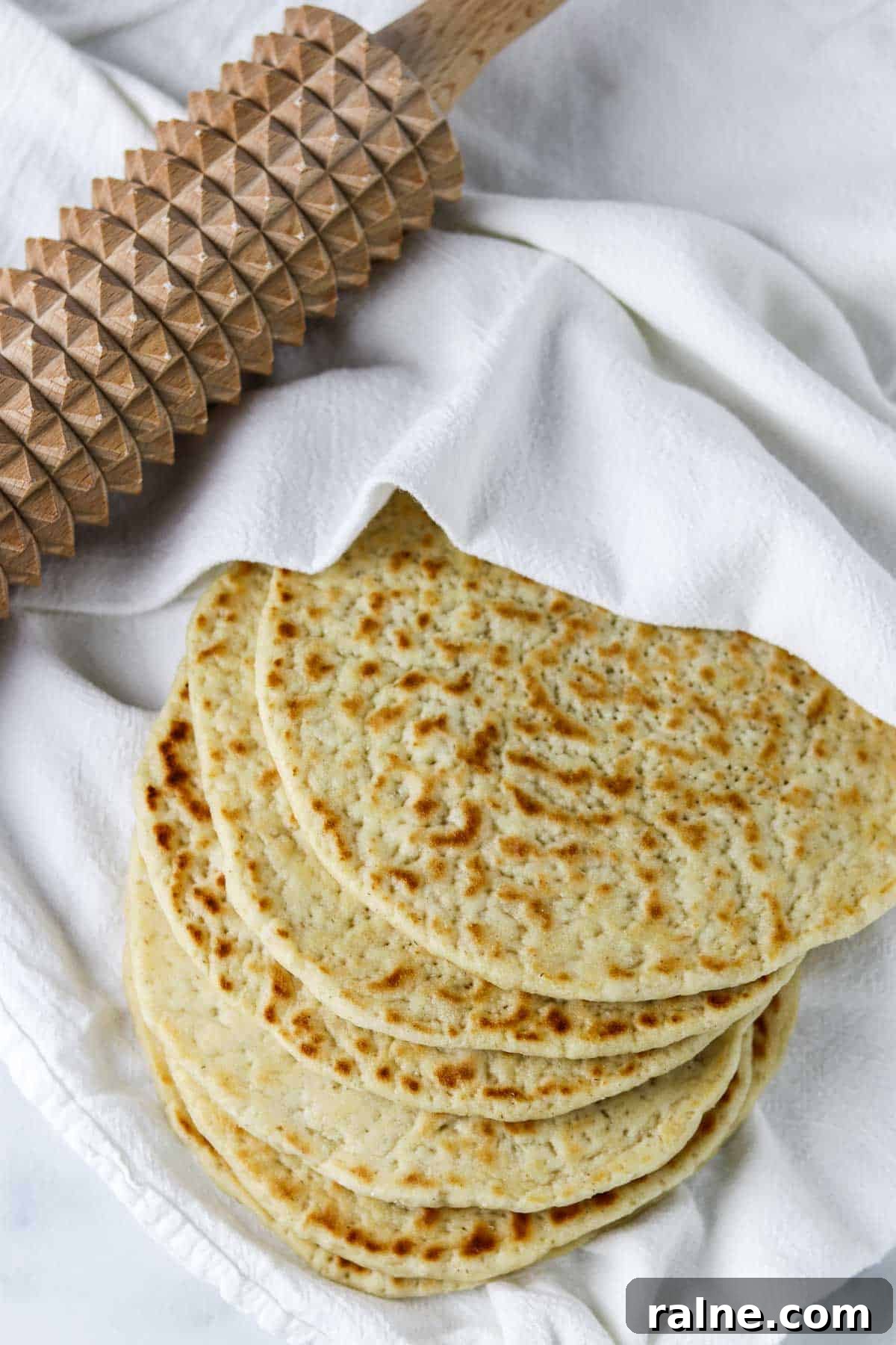Soft Swedish Tunnbröd Recipe: How to Make Traditional Flatbreads 13 Flatbreads on a towel next to a spiked rolling pin.