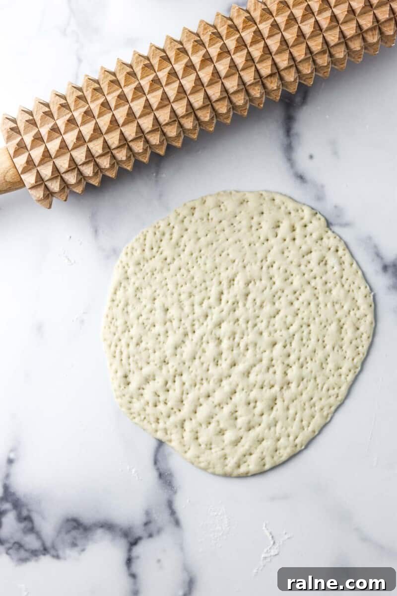 Soft Swedish Tunnbröd Recipe: How to Make Traditional Flatbreads 8 Flatbread dough rolled out on a marble counter with a spiked rolling pin.