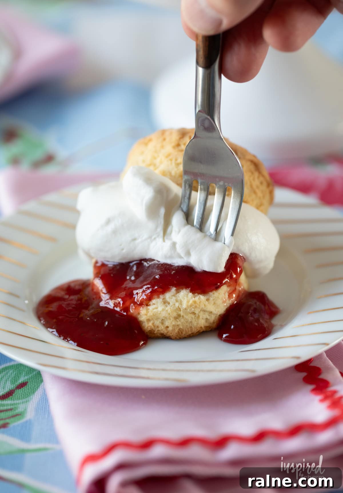 hand with folk taking a bite of scone filled with jam and whipped cream.