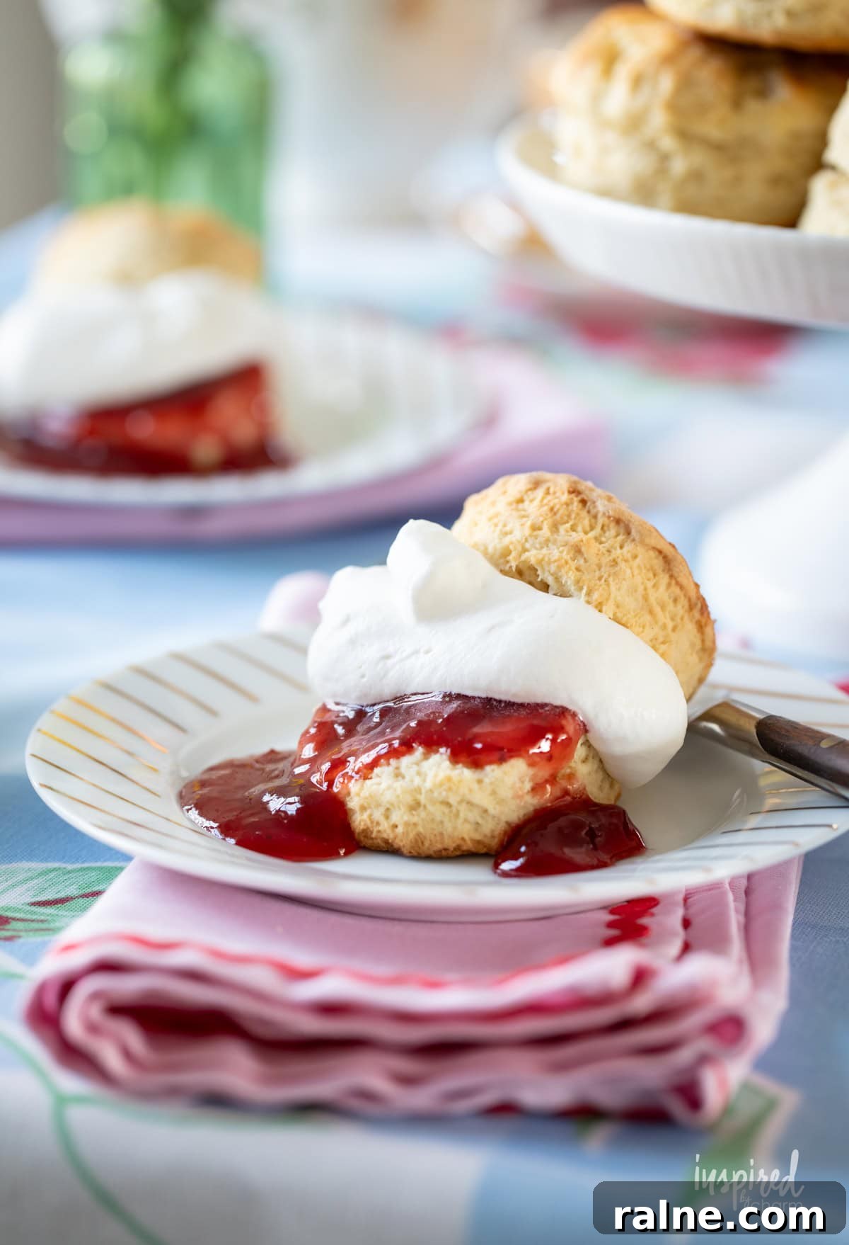 scone served with whipped cream and strawberry jam on a plate with a fork. 