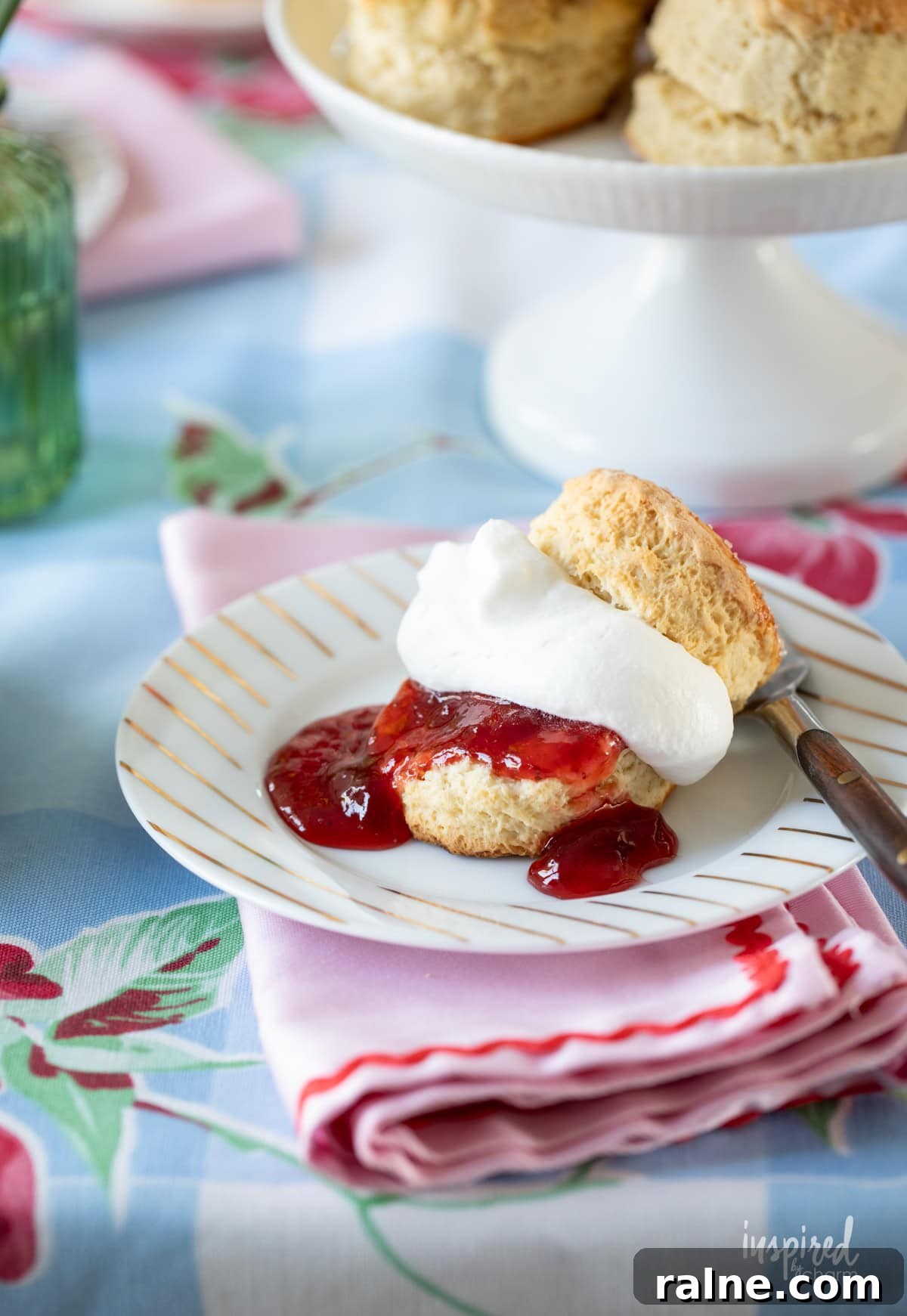 single scone cut in half filled with strawberry jam and whipped cream. 