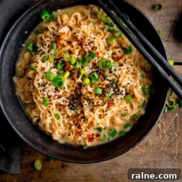 Singapore Stir-Fry Noodles with Curry and Shrimp 10 Overhead square image of a black bowl filled with ramen noodles topped with chilli flakes, spring onions and mixed sesame seeds.