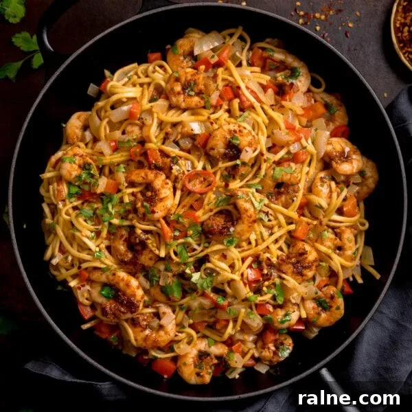 Singapore Stir-Fry Noodles with Curry and Shrimp 14 A frying pan filled with king prawn stir-fry noodles, featuring prawns, noodles, diced red peppers, onions, and garnished with chopped herbs.