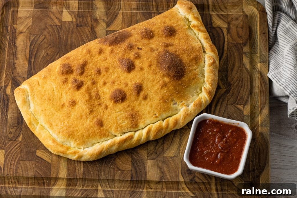 browned calzone on a wooden cutting board with a small bowl of pizza sauce