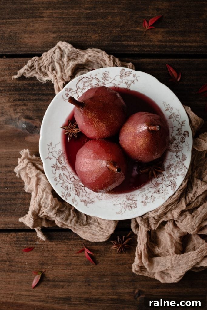 Wine-Poached Pears Recipe: Elegant Dessert with Red Wine Glaze 4 Poached Red anjou pears on plate with red sauce.