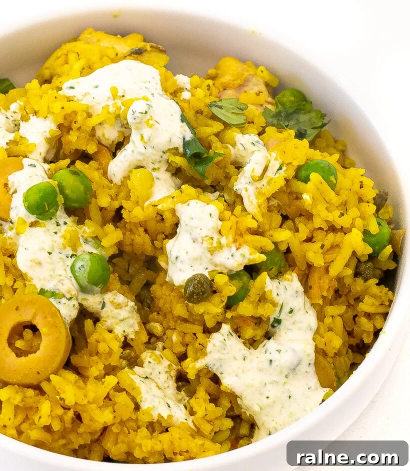 Authentic Latin-Style Chicken and Rice Recipe 11 Arroz con pollo served in a white bowl with the sauce drizzled on top.
