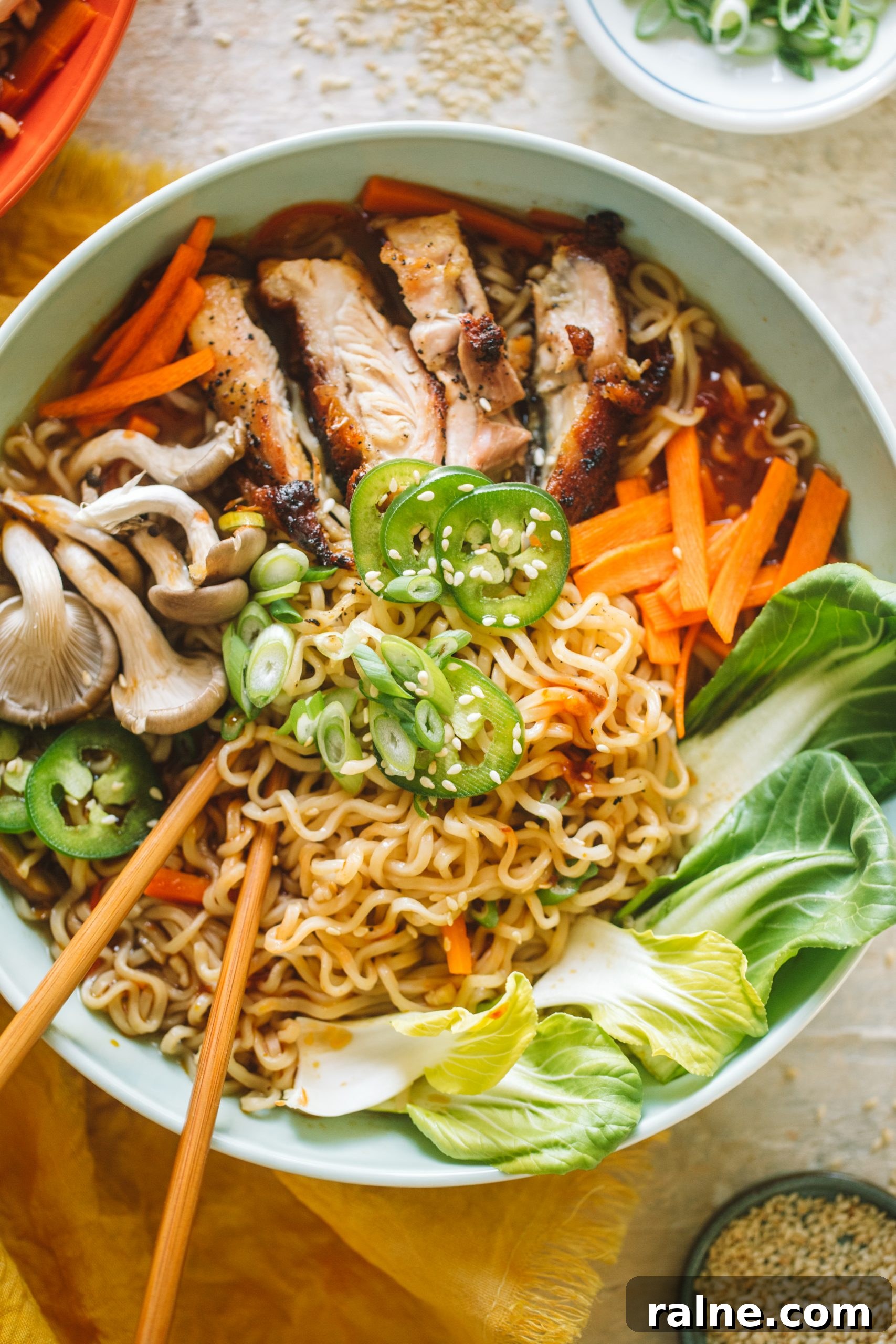 Spicy chicken ramen topped with jalapenos, mushrooms, bok choy, carrots and served in a blue bowl.