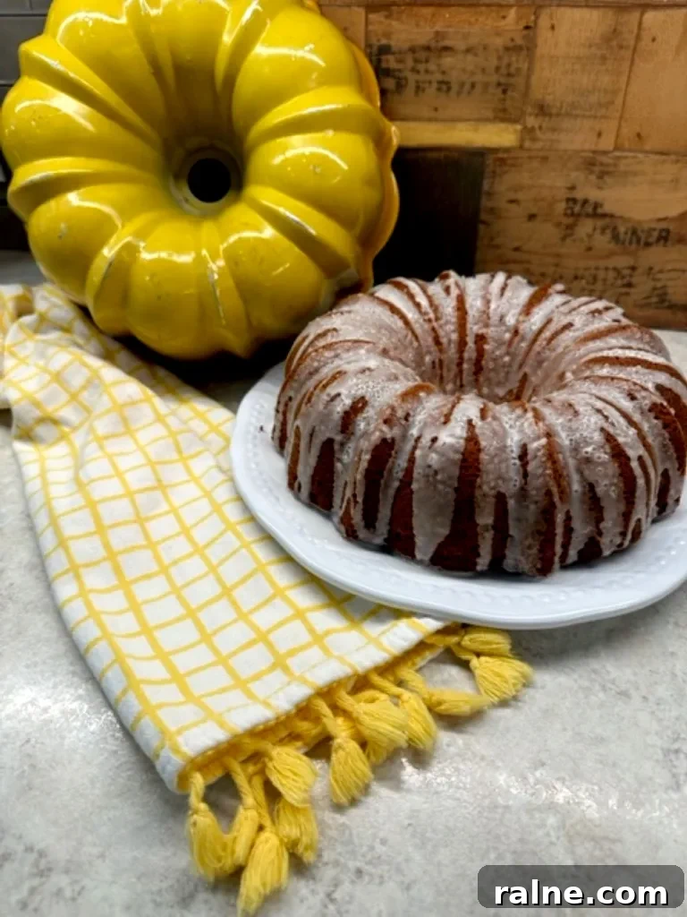 Golden yellow Bundt pan next to a powdered sugar–dusted Mountain Dew Bundt cake on a patterned kitchen towel.