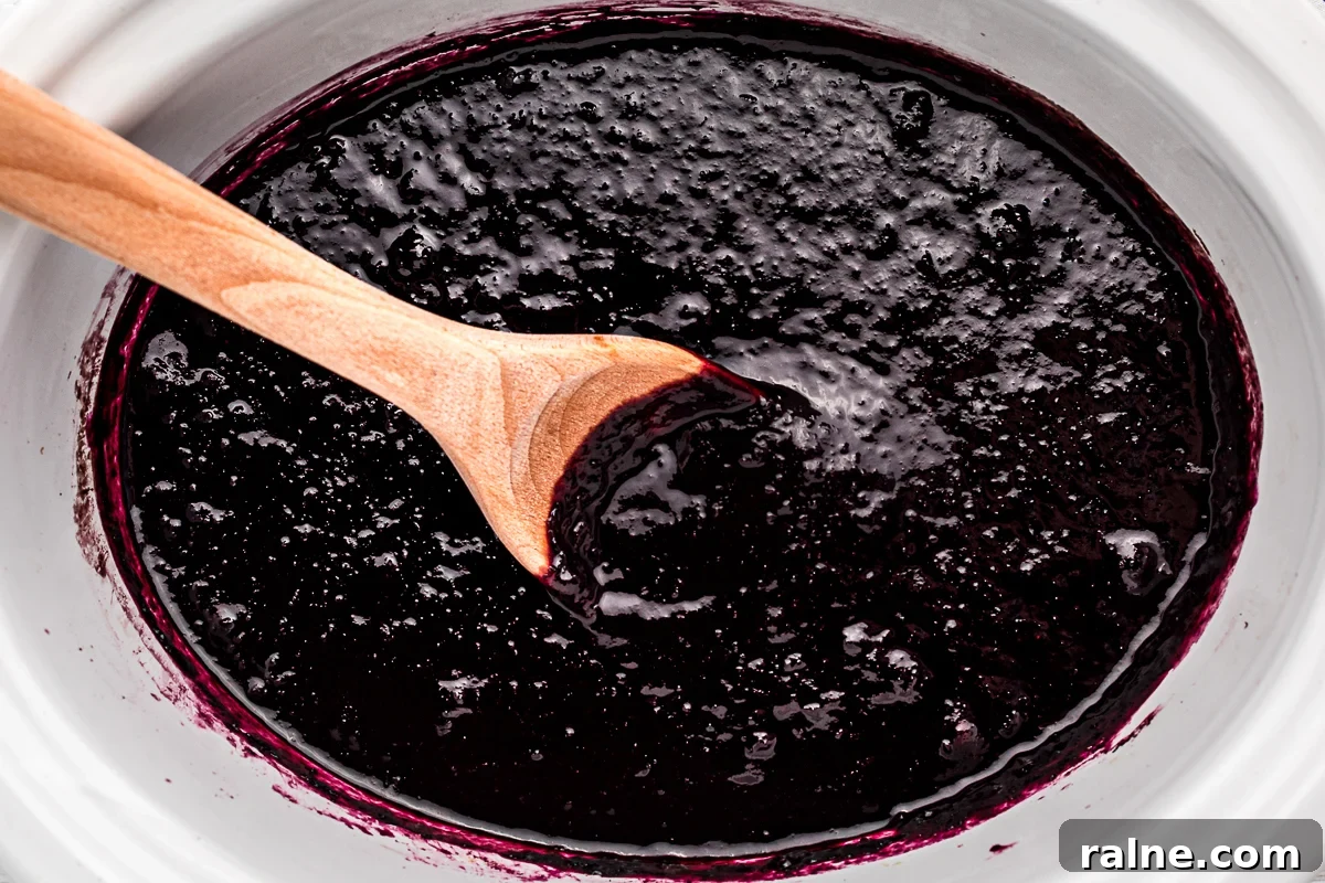 How to Make Homemade Blueberry Butter (Smooth & Spreadable) 5 close up of blueberry butter with wooden spoon in it.